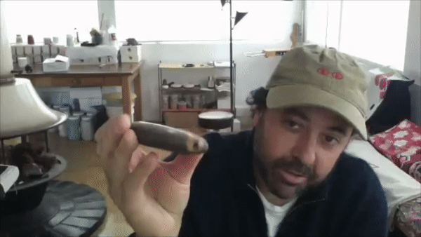 A person holds up a ceramic pipe.